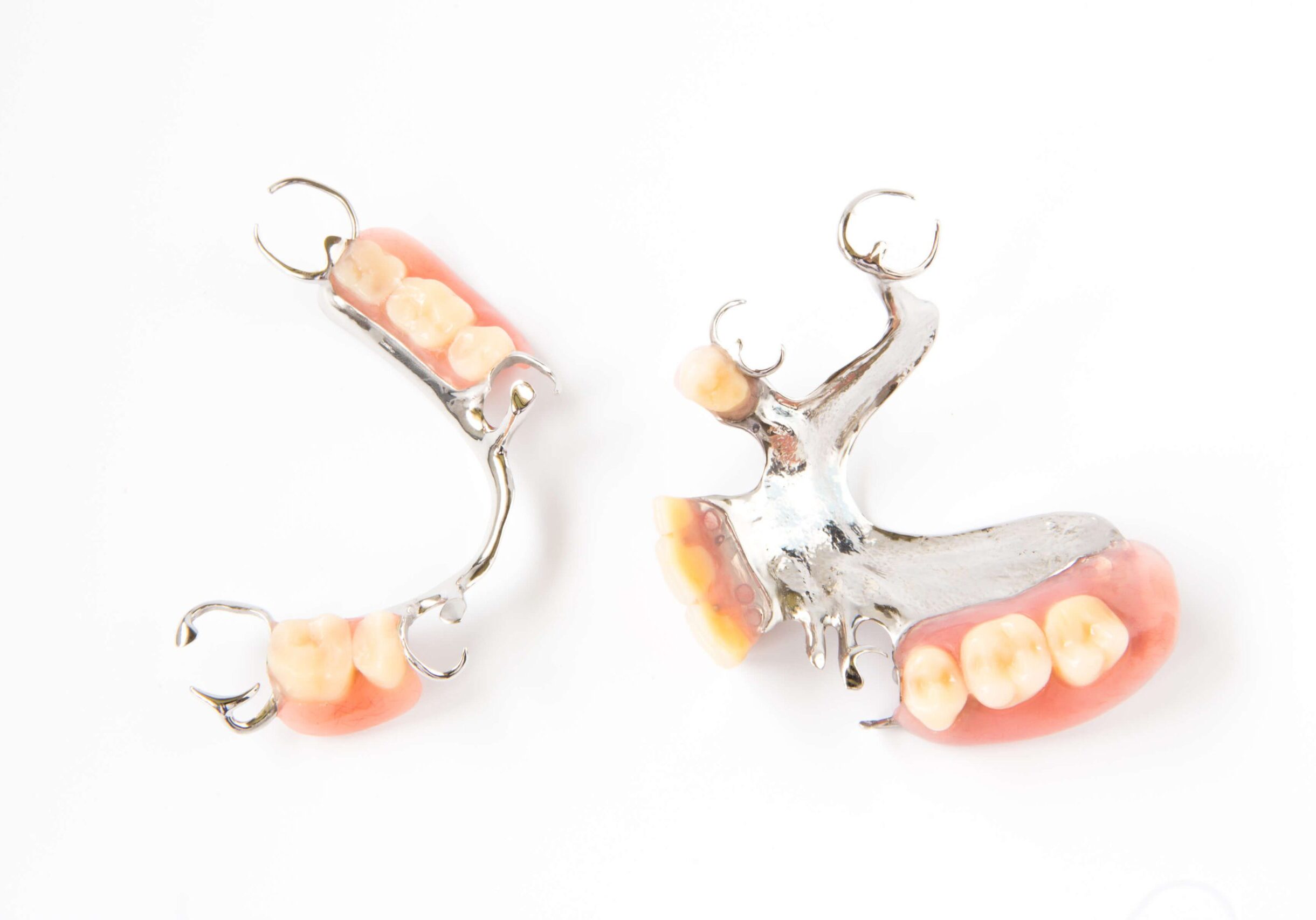 GettyImages-680220254 Two partial dentures with metal frameworks and artificial teeth on a white background.